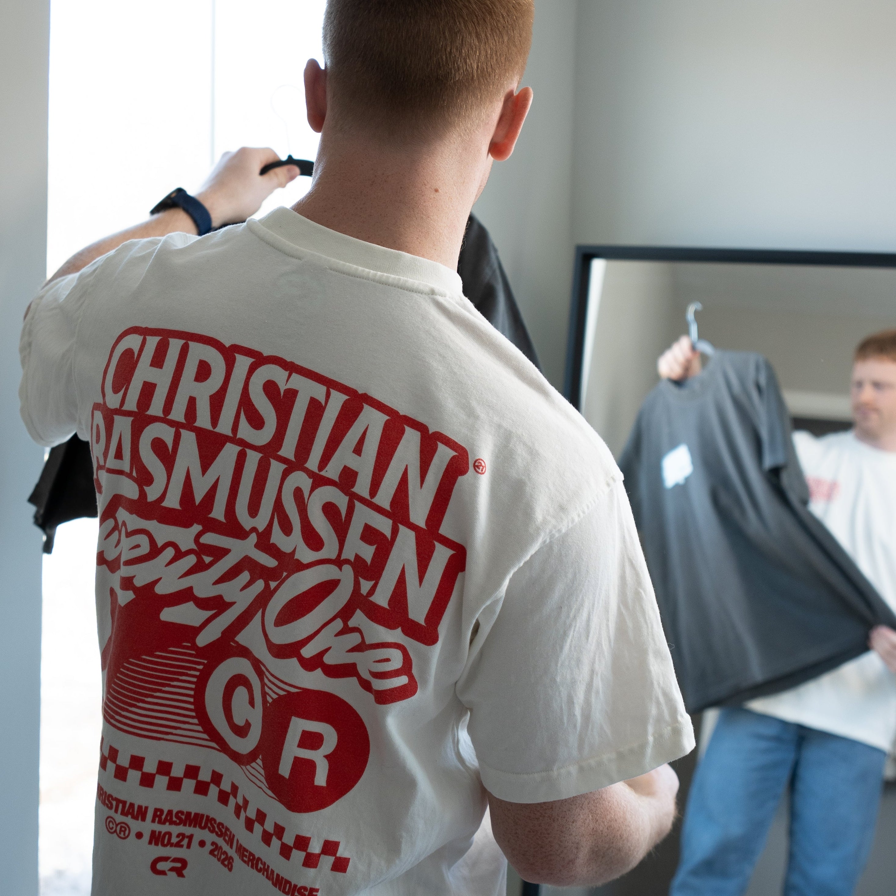 Person wearing a white t-shirt with red text in a room setting