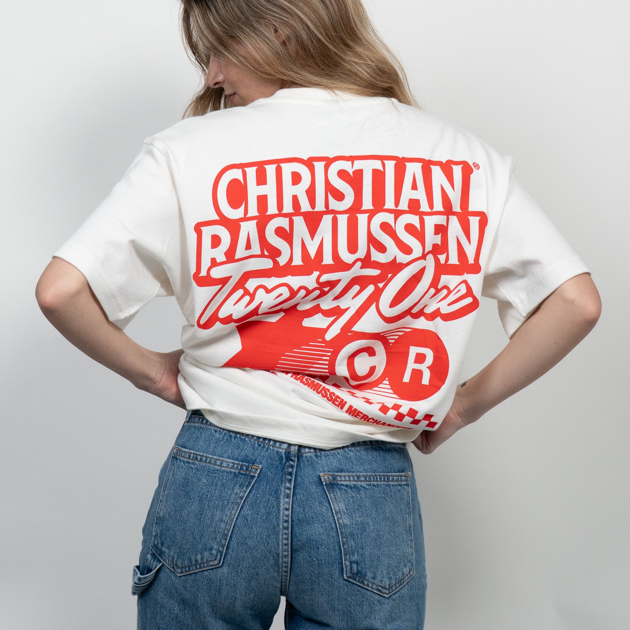 Person wearing a white t-shirt with red text and design on the back, standing against a plain background.