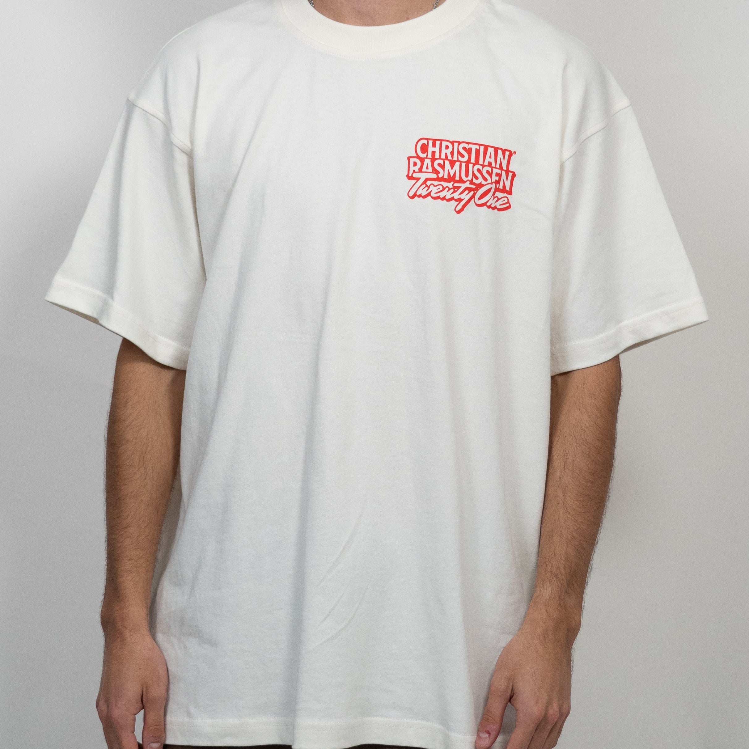 Person wearing a white t-shirt with a red logo on a plain background