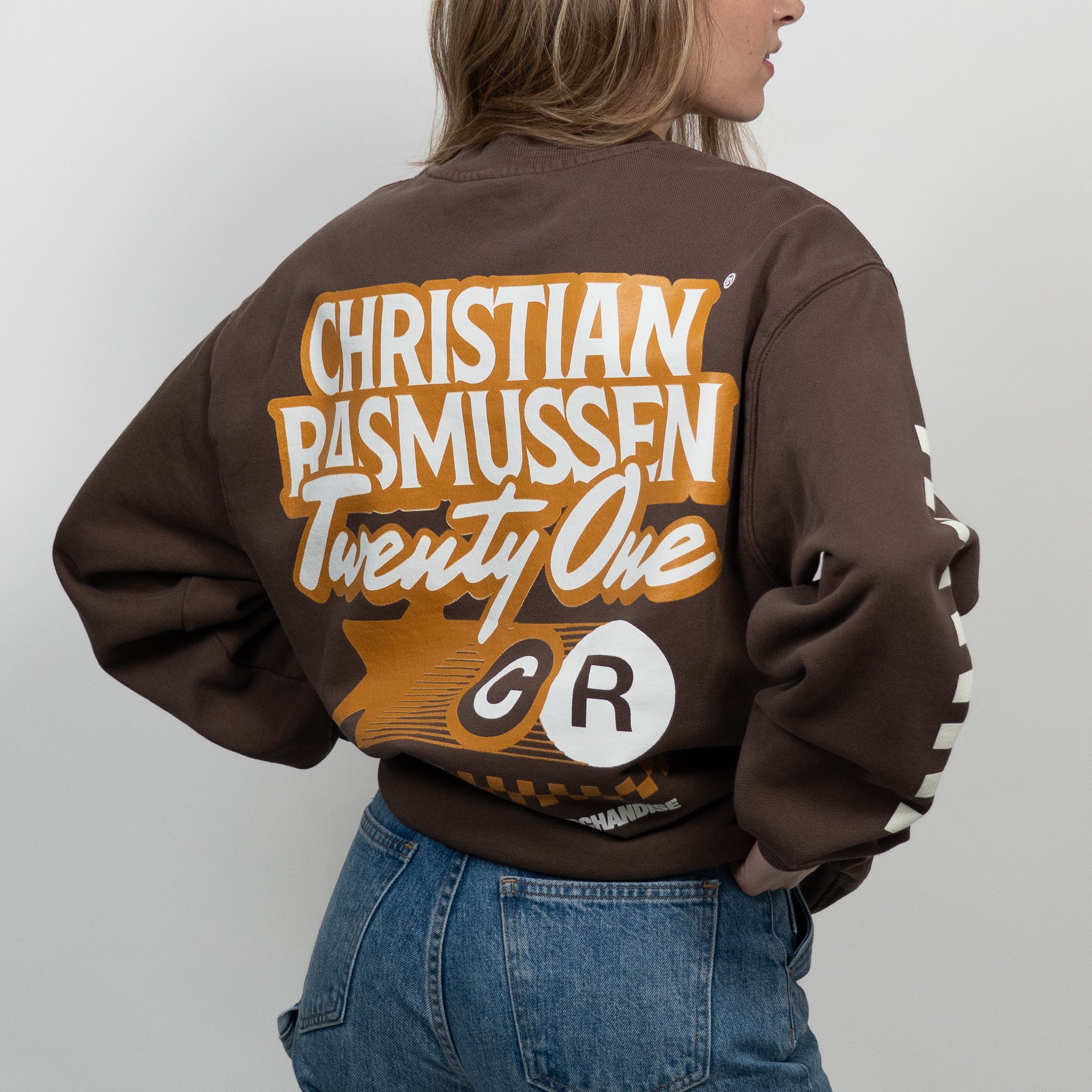Person wearing a brown sweatshirt with 'Christian Rasmussen Twenty One' text on the back, standing against a plain background.