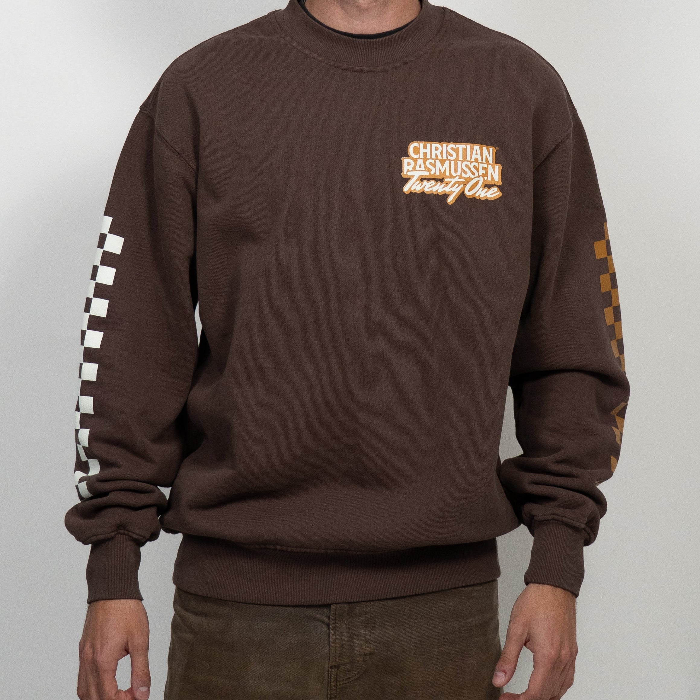 Person wearing a brown sweatshirt with visible branding on a white background