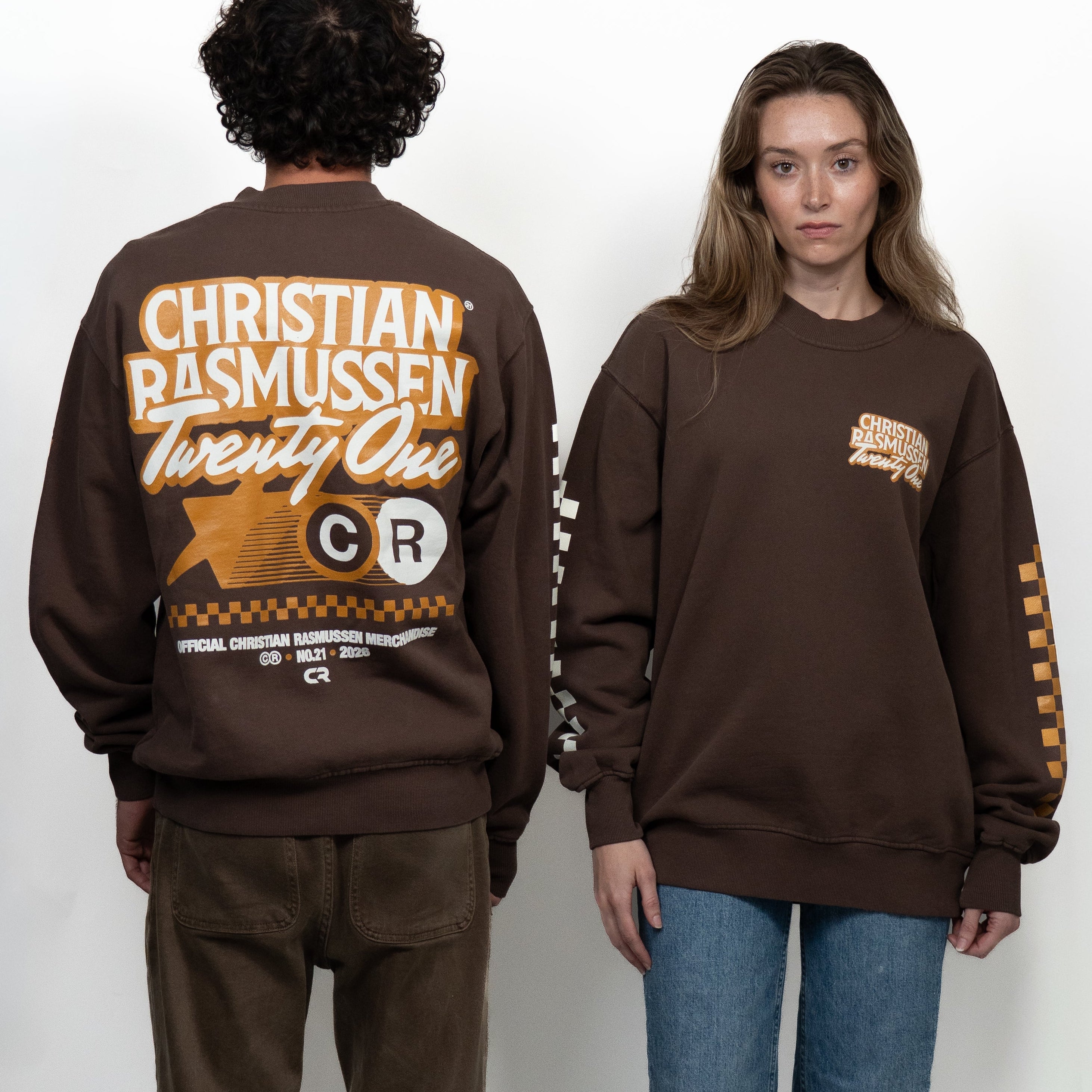 Two people wearing brown sweatshirts with visible branding on a white background