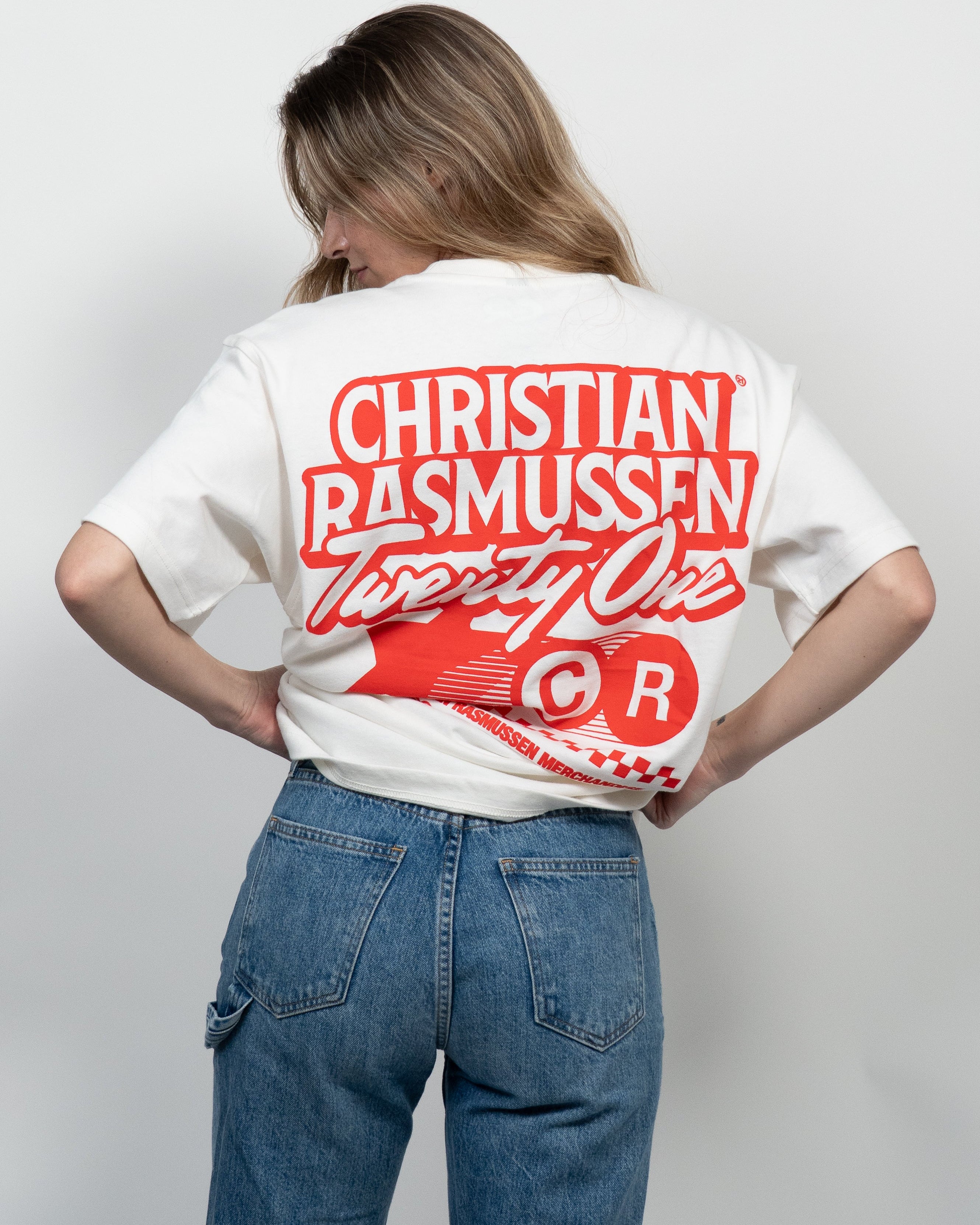Person wearing a white t-shirt with red text and design on the back, standing against a plain background.
