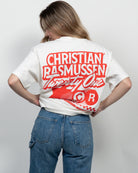 Person wearing a white t-shirt with red text and design on the back, standing against a plain background.