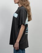 Person wearing a black t-shirt with graphic designs on a plain background