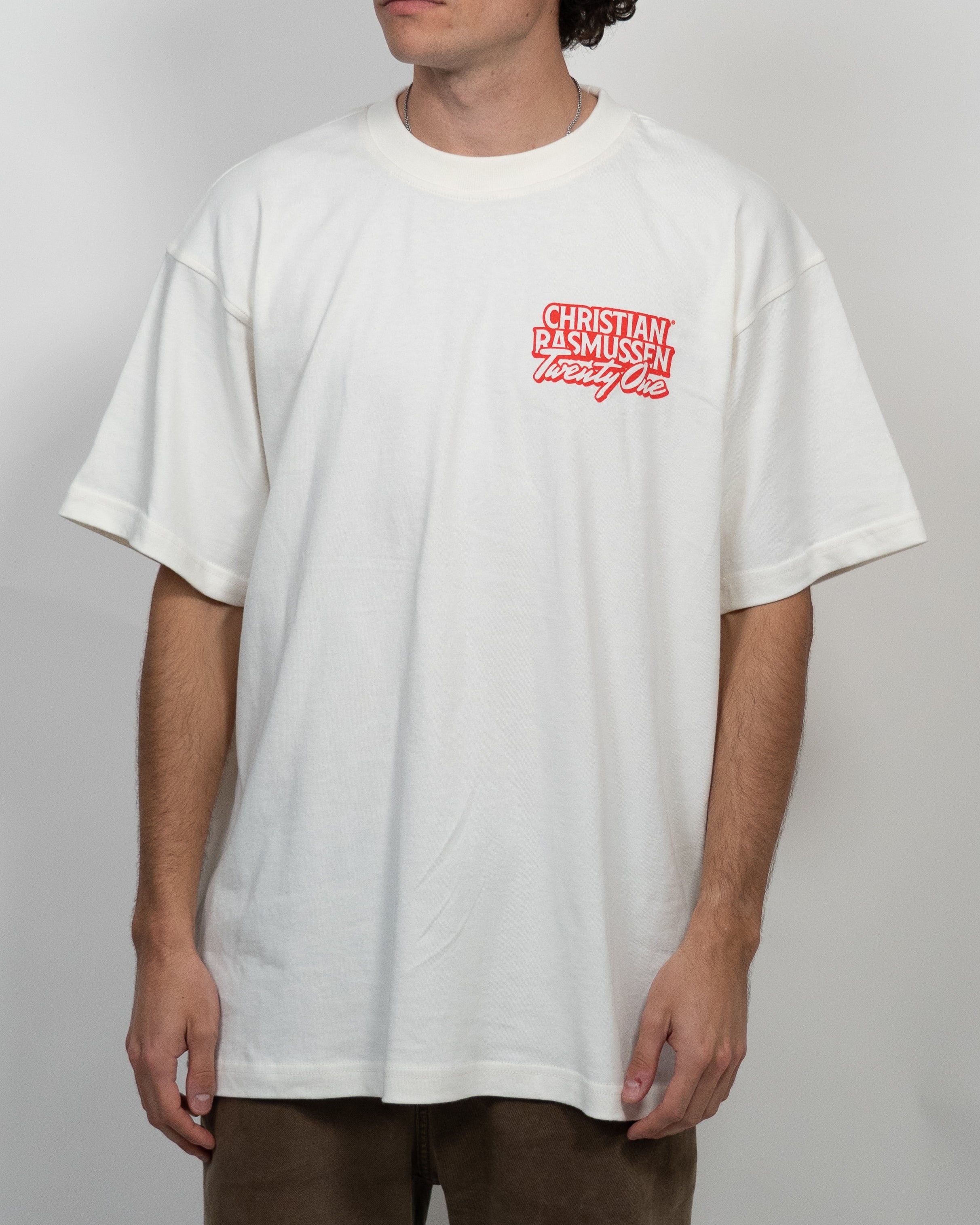 Person wearing a white t-shirt with a red logo on a plain background