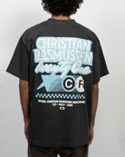 Person wearing a black t-shirt with blue and white text and graphics on the back, against a plain background.