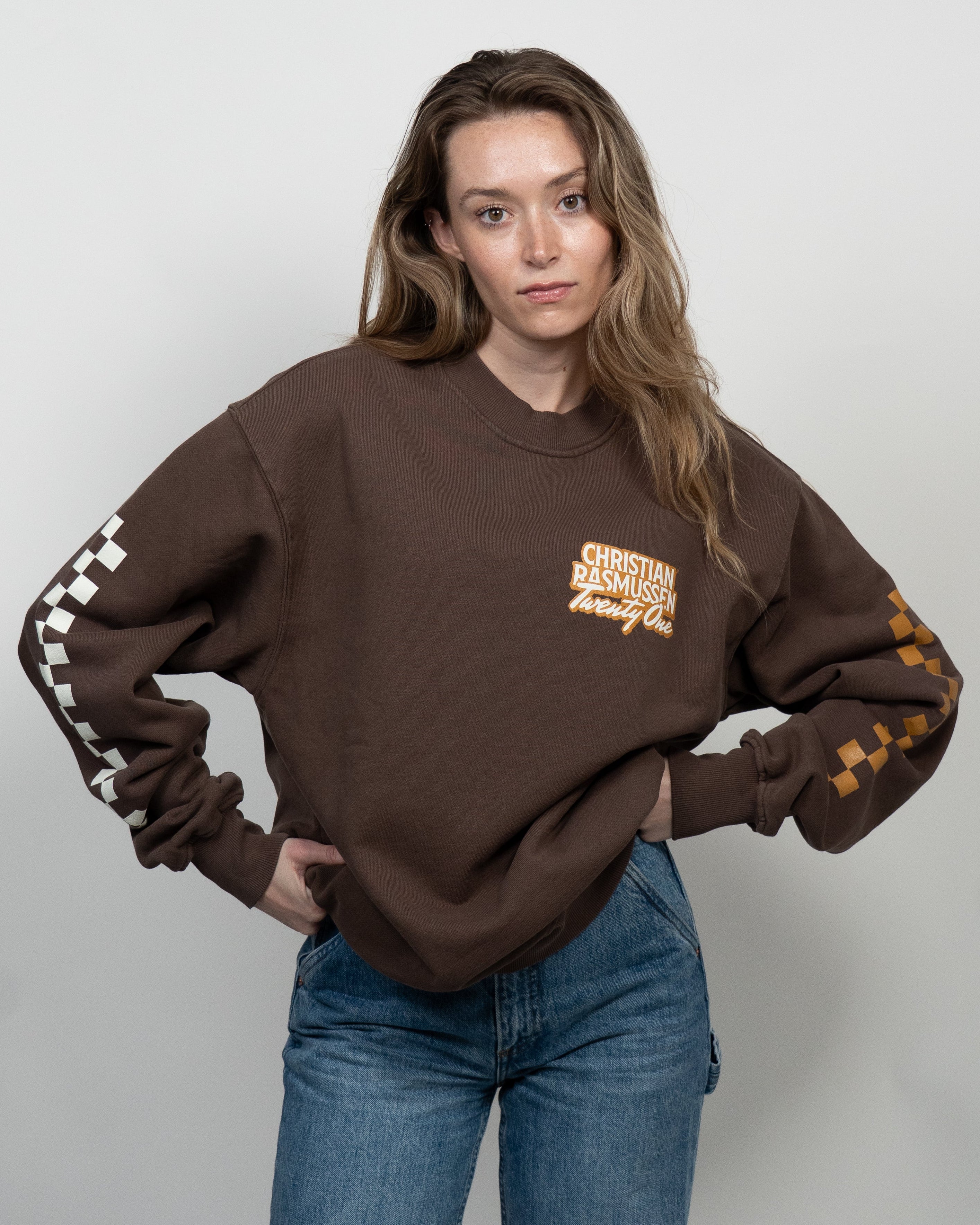 Person wearing a brown sweatshirt with text and graphics on sleeves against a plain background