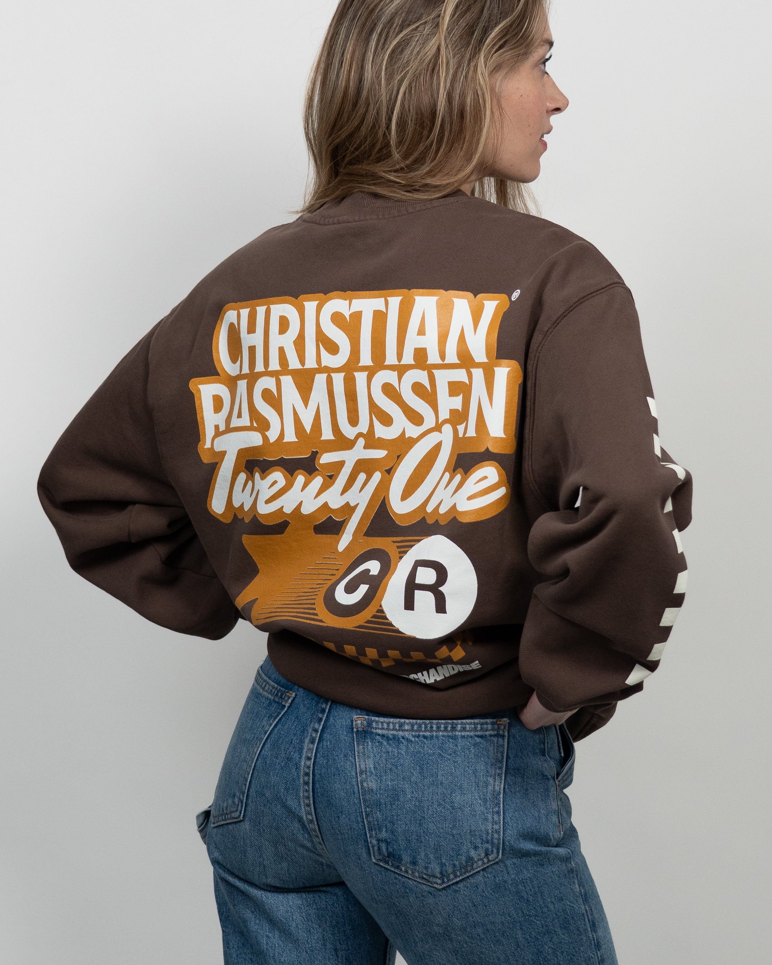 Person wearing a brown sweatshirt with 'Christian Rasmussen Twenty One' text on the back, standing against a plain background.