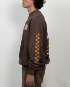 Man wearing a brown sweatshirt with checkered pattern on sleeves against a white background