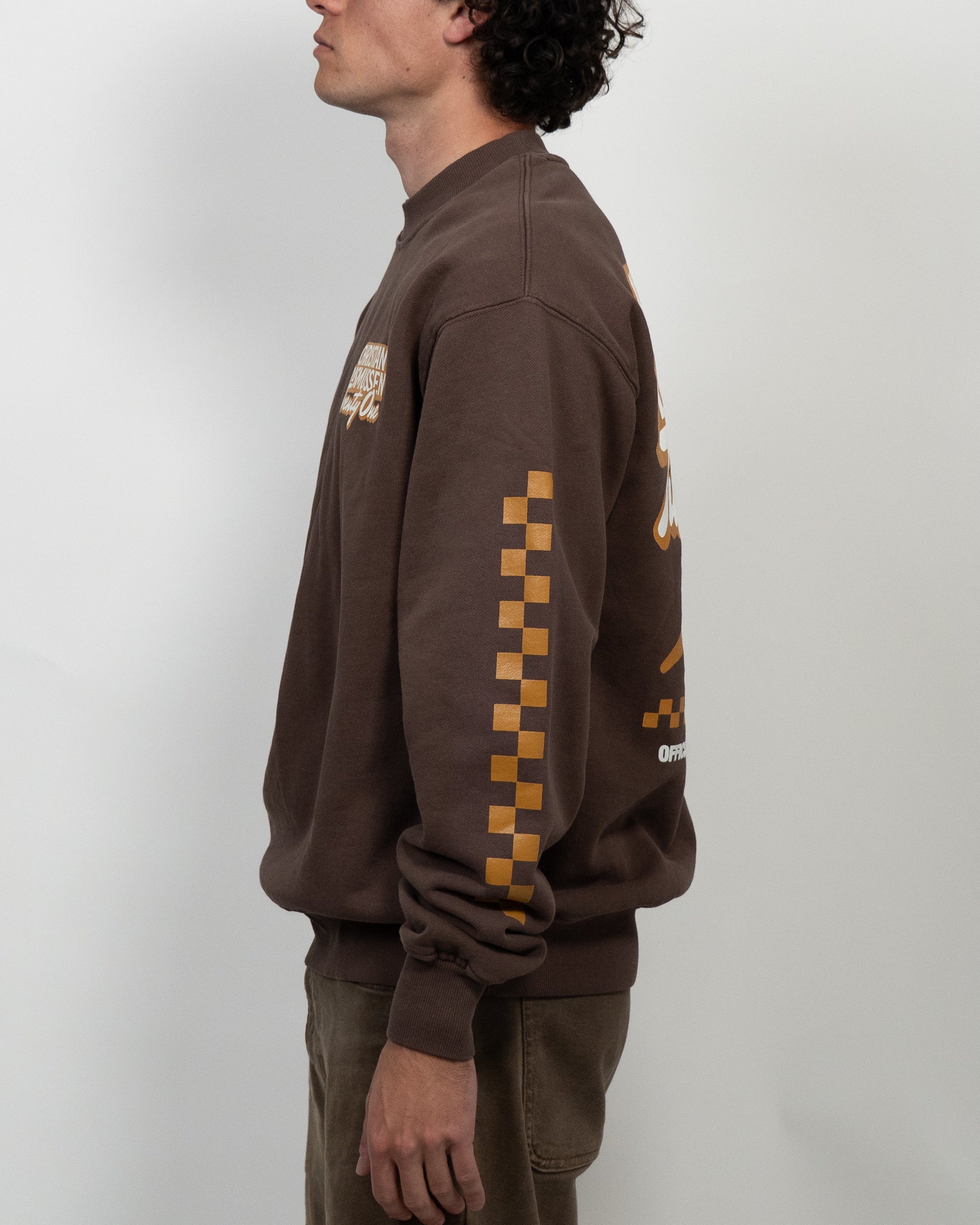 Man wearing a brown sweatshirt with checkered pattern on sleeves against a white background