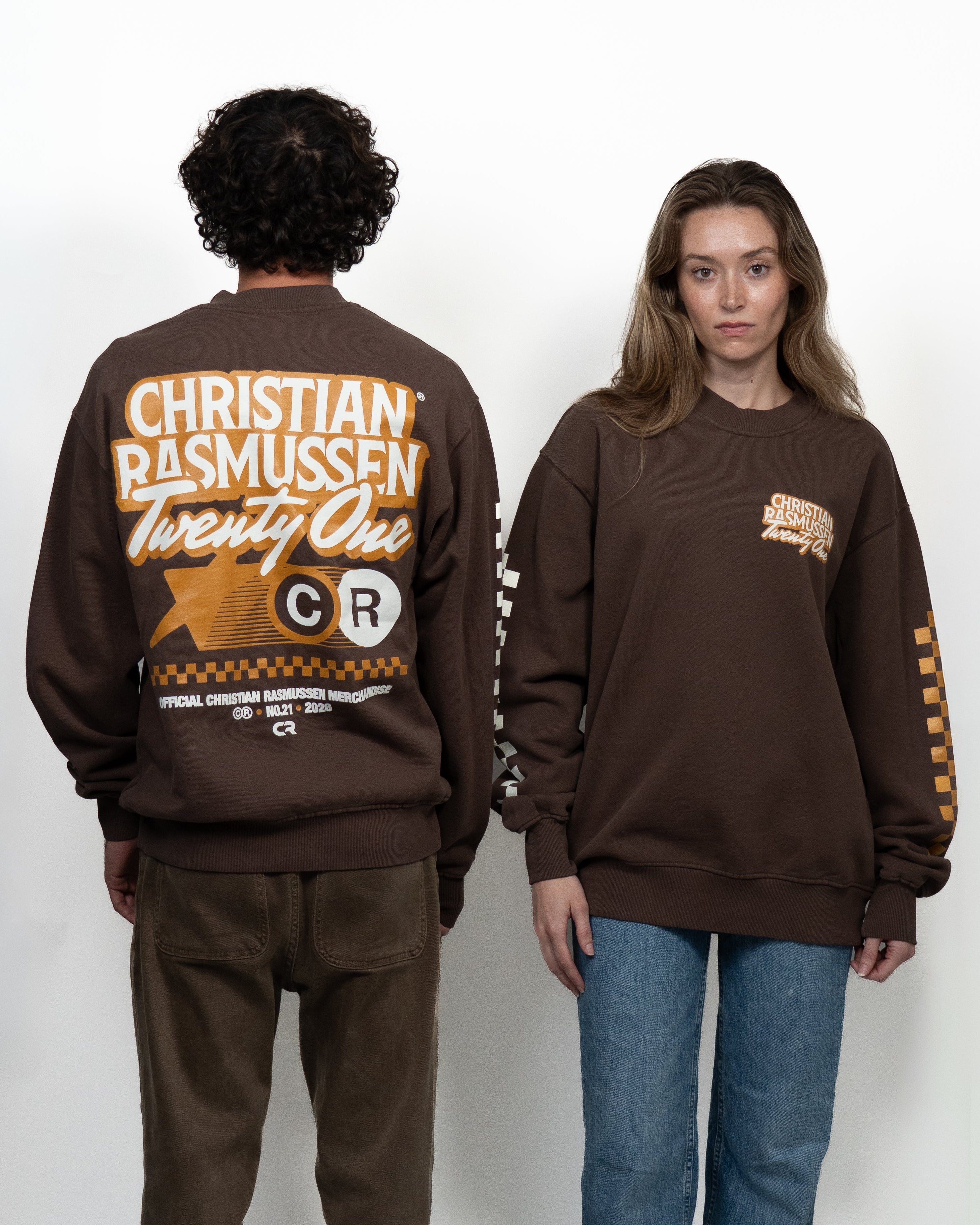 Two people wearing brown sweatshirts with visible branding on a white background
