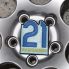 Close-up of a car wheel with a '21 Rasmussen' badge on a textured pavement background